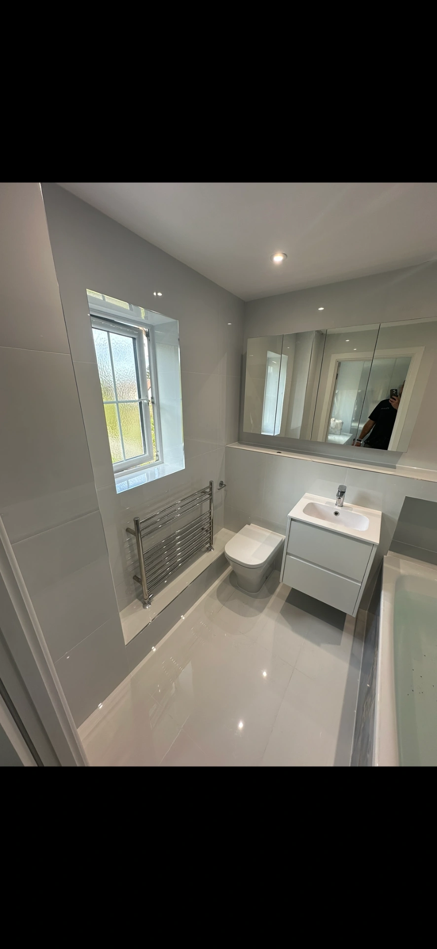 Bright white family bathroom with floating vanity, mirrored cabinet and gloss floor tiles — bathroom installation in Sunningdale