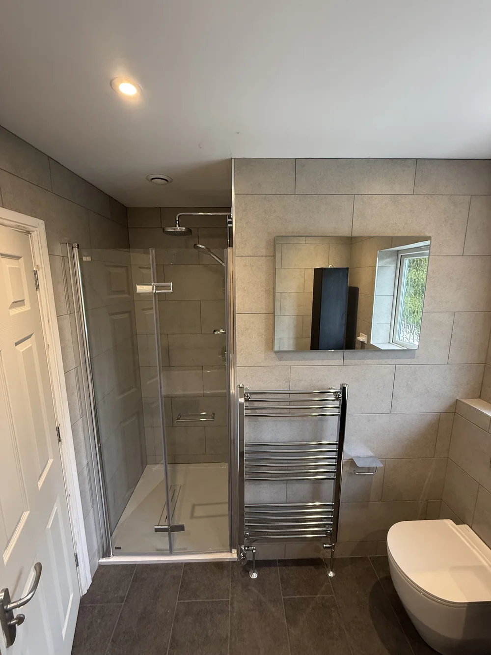 Stone-tiled family bathroom with hinged glass shower enclosure and chrome towel rail — bathroom installation in Sunningdale