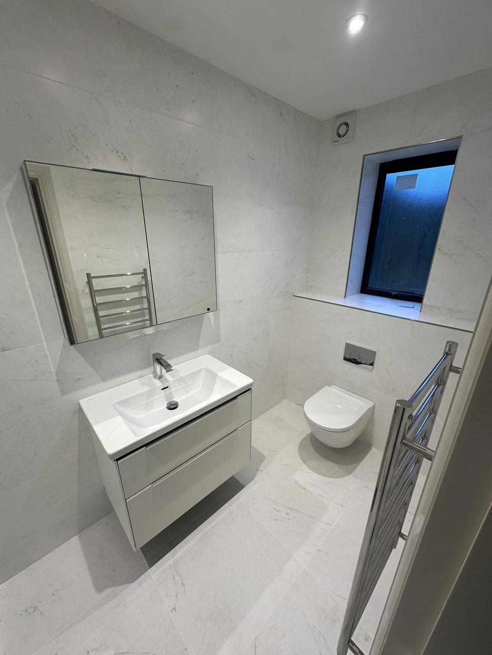 White marble ensuite with wall-hung vanity, mirrored cabinet and back-to-wall WC — Sunningdale, Berkshire