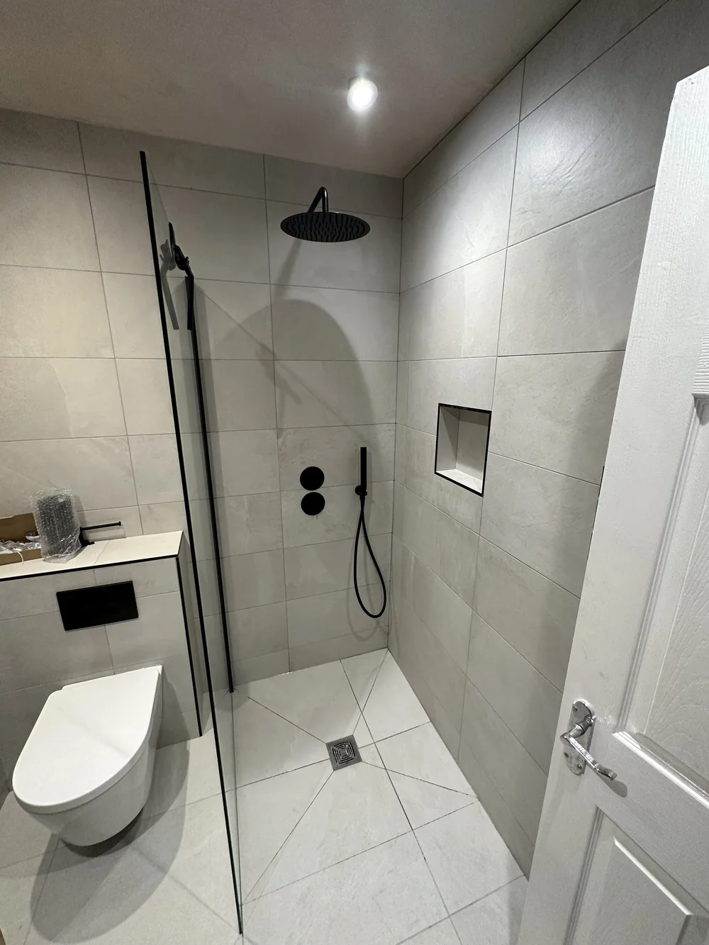 Stone-tiled walk-in shower with matte black rainfall head and recessed niche — wet room in Sunningdale