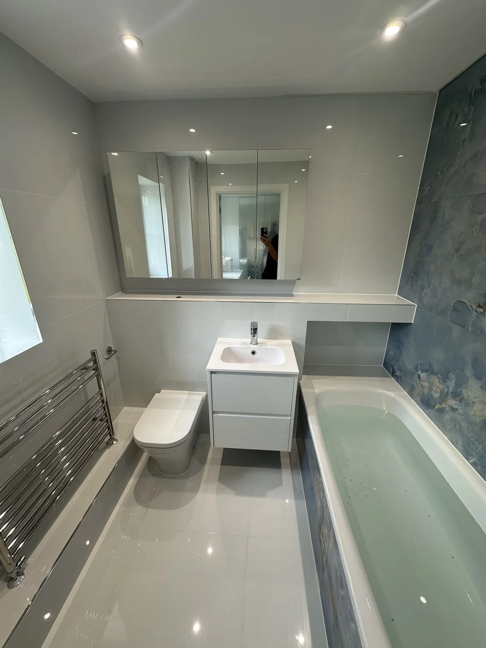 Bright family bathroom with mirrored cabinet, white vanity and blue onyx accent wall — bathroom renovation in Sunningdale