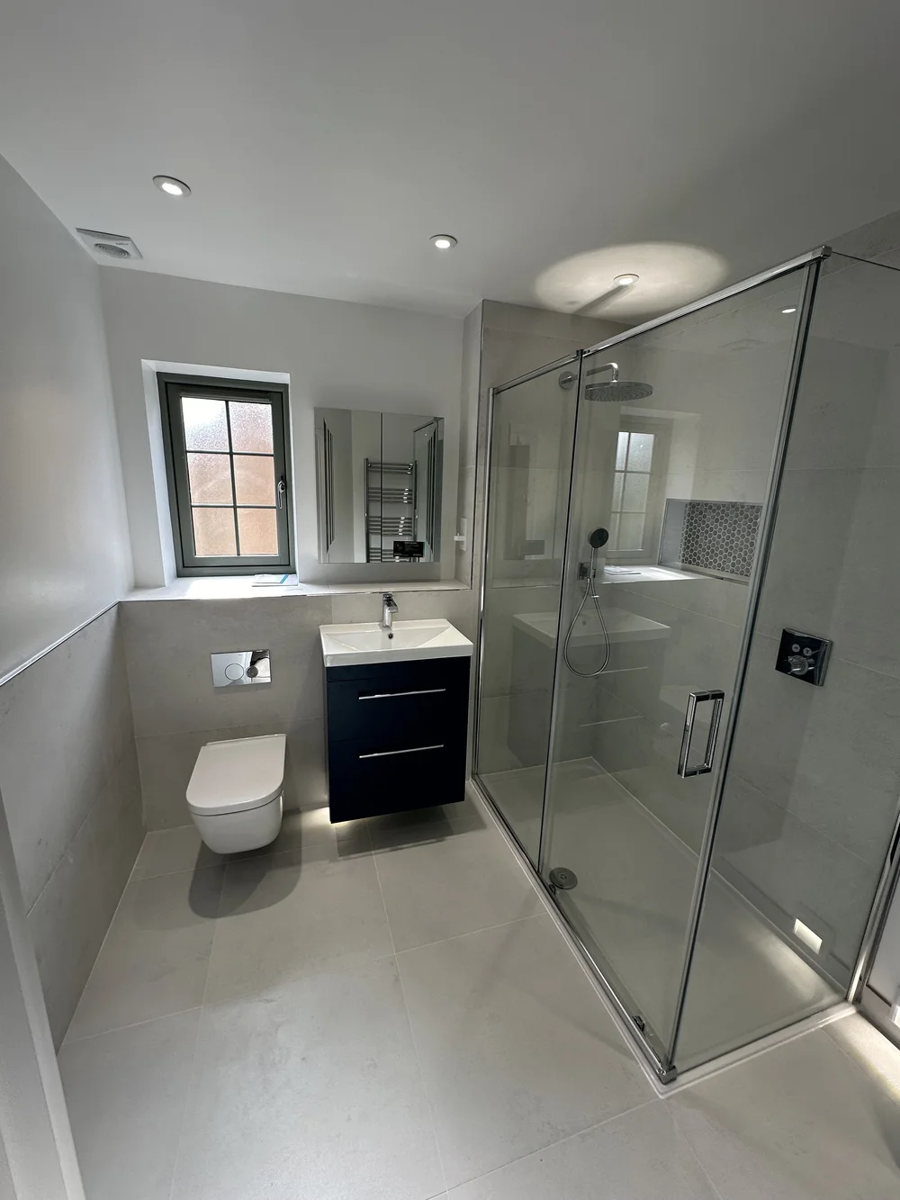Fitted shower room with navy vanity, wall-hung WC and large glass shower enclosure — bathroom installation in Sunningdale