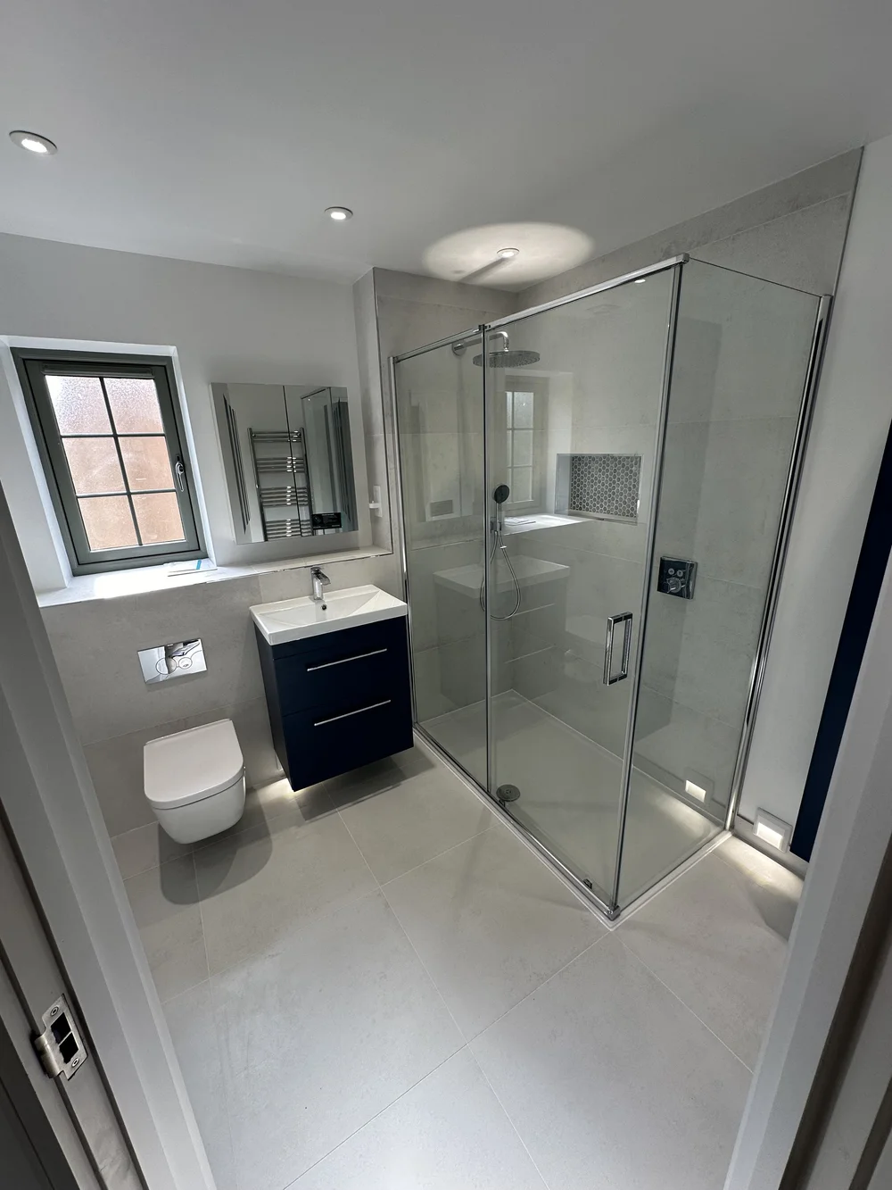 Fitted ensuite with navy vanity, wall-hung WC and corner shower enclosure — bathroom installation in Sunningdale